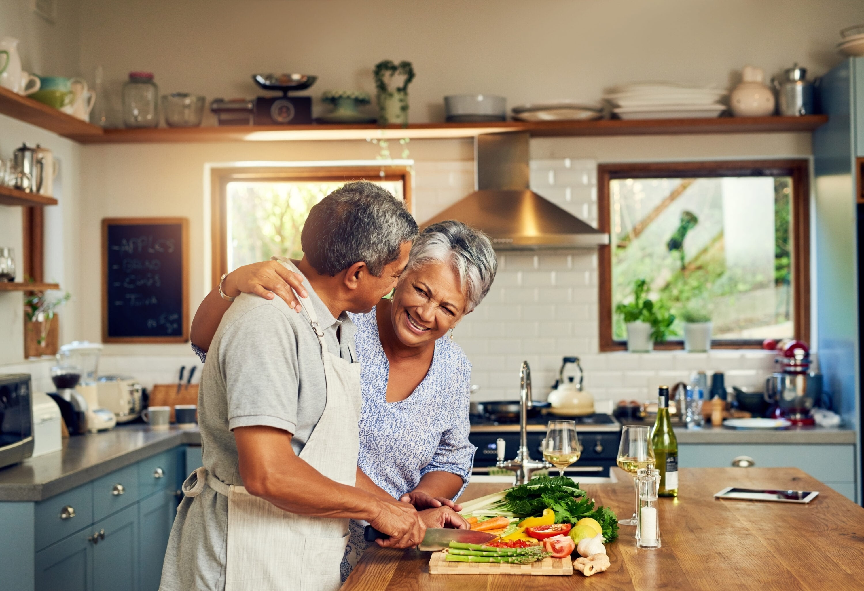 Mature man and woman in a kitchen smiling and cooking food together.