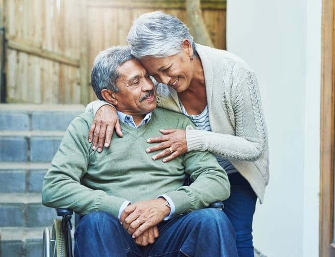 Woman hugs an elderly man seated in a wheelchair at Brightwater Senior Living