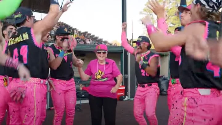 Baseball players in pink uniforms celebrate with woman