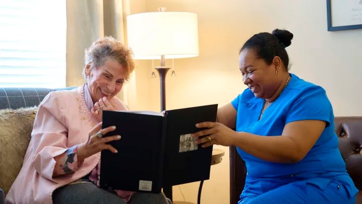 Two women smiling at photo album indoors