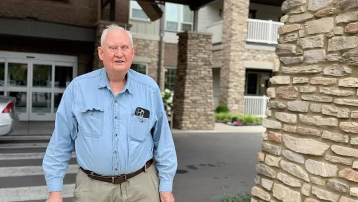 Elderly man standing outside stone building entrance