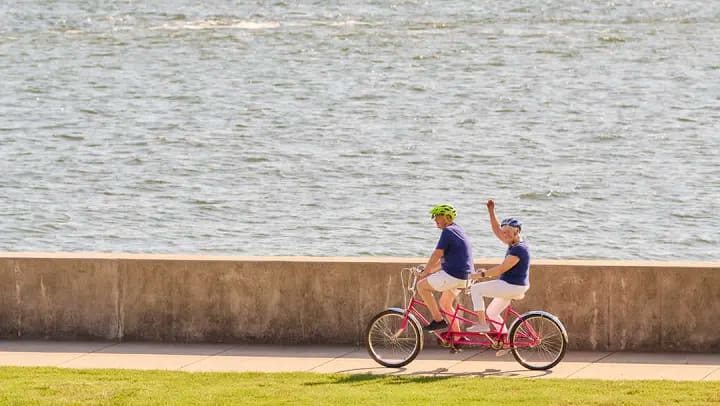 Two people riding tandem bicycle by waterfront