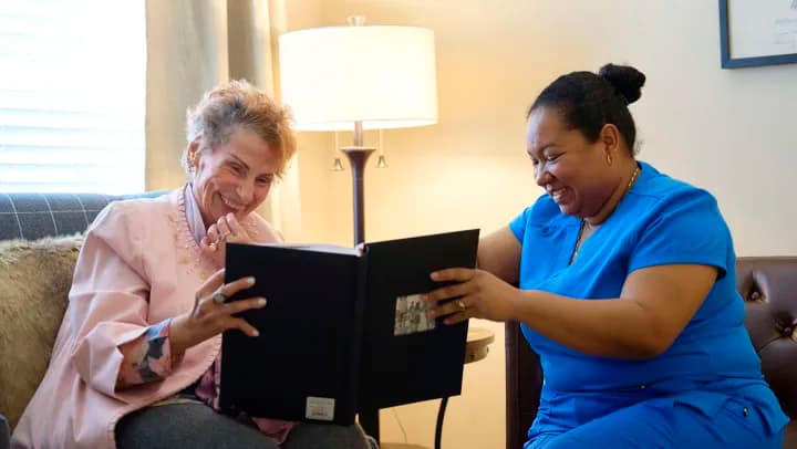 Two women smiling at photo album indoors