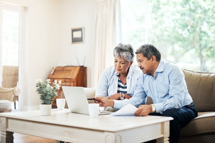 Two seniors sitting on a couch going over paperwork and studying information on a computer at Brightwater Senior Living of Tuxedo in Winnipeg, Manitoba