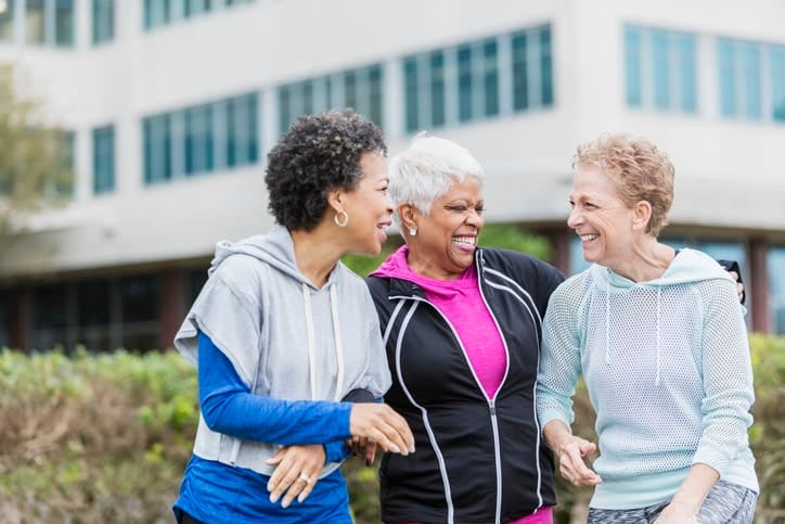 Three senior women wearing sweatshirts laughing and talking while they take a walk in the neighborhood near Brightwater Senior Living