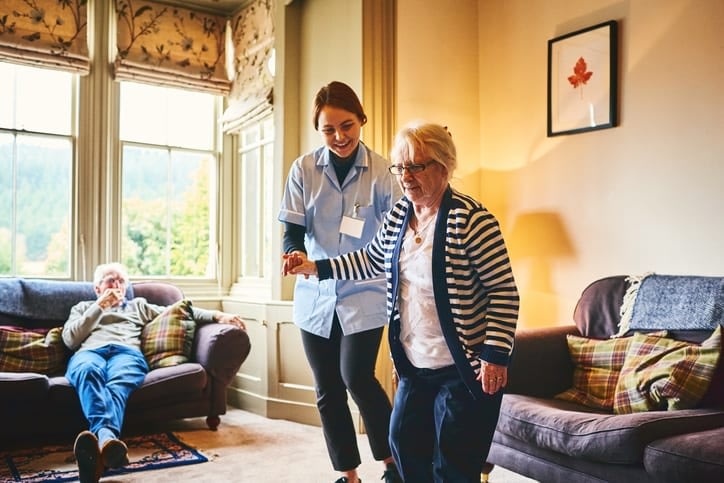 Nurse supports a senior woman as she walks indoors at Brightwater Senior Living